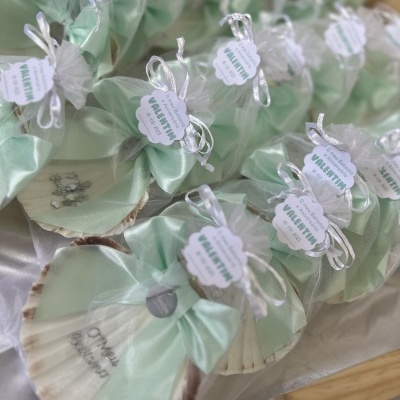 Lembranças em saquinhos transparentes com fita verde e etiquetas brancas, contendo conchas decoradas.