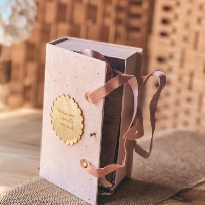 Caixa rosa com alça de couro e placa dourada com texto