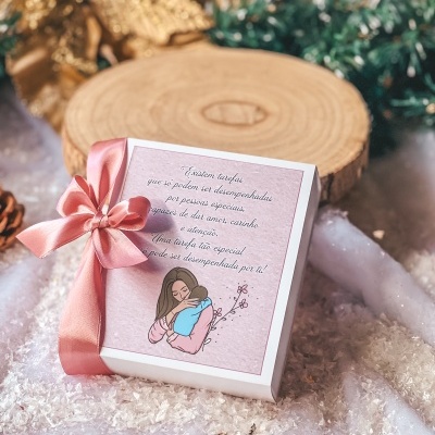 Caixa presente com laço rosa e mensagem em português, junto a decoração natalícia e superfície branca