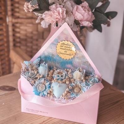 Envelope rosa com flores artificiais azuis e placa dourada com texto em português