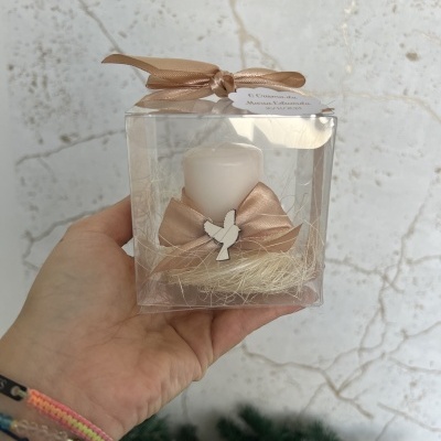 Vela pequena branca com laço bege e enfeite de anjo em embalagem transparente