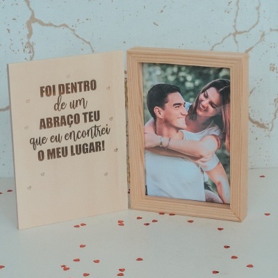 Porta-retratos em madeira com frase gravada e foto de casal sorridente, sobre superfície branca com corações vermelhos