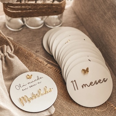 Placas redondas brancas decorativas com texto e borboletas douradas sobre tecido rústico