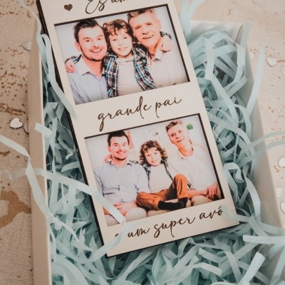 Cartão branco com duas fotos e texto dourado dentro de caixa com papel de seda azul