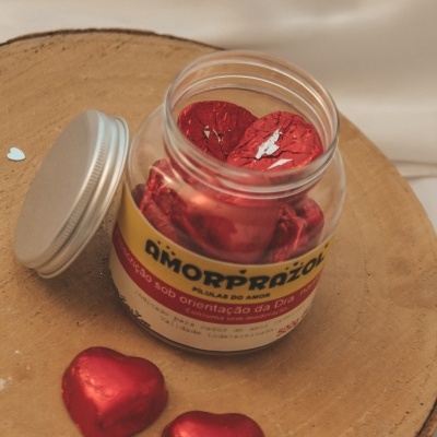 Frasco com balas vermelhas em forma de coração sobre base de madeira