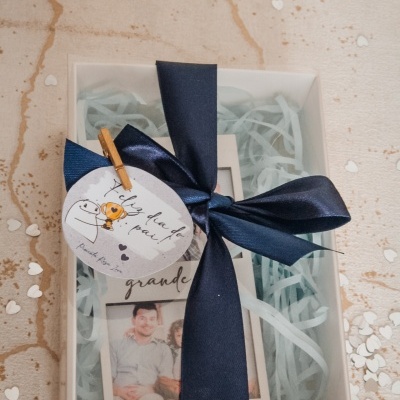 Caixa branca com fita azul, cartão com texto dia do pai, moldura com foto dentro.