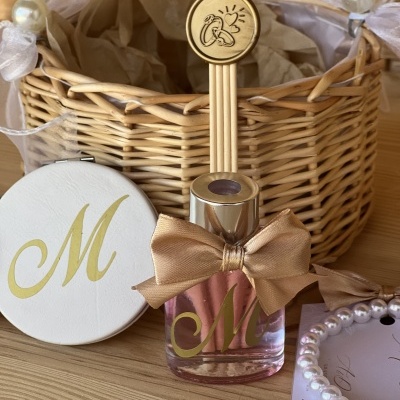 Difusor de aroma rosa com laço dourado e letras M, cesto de vime com alças de pérolas, estojo branco e pulseira de pérolas