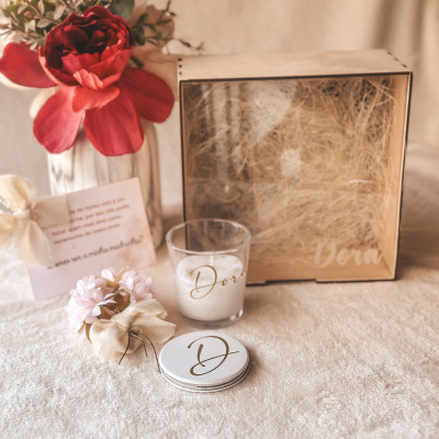 Conjunto de vela e caixa decorativa com flores e cartão sobre tecido creme.