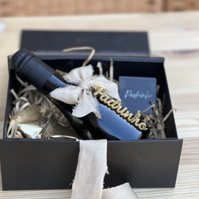 Caixa de oferta preta com garrafa preta decorada com laço bege e placa dourada 'Padinho'