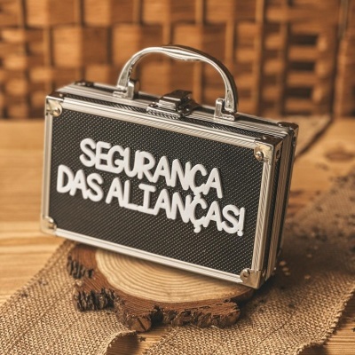 Mala metálica pequena preta com texto branco SEGURANÇA DAS ALIANÇAS e fundo em madeira.