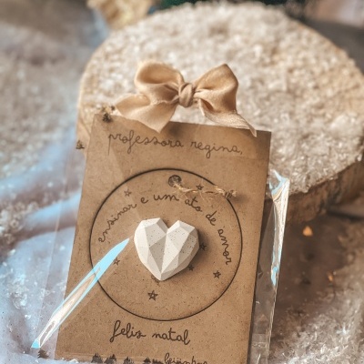 Cartão castanho com laço dourado e coração branco facetado em embalagem plástica com texto manuscrito