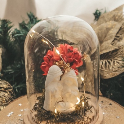 Presépio branco dentro de campânula de vidro decorativa de Natal com luzes LED e flor vermelha numa base de madeira