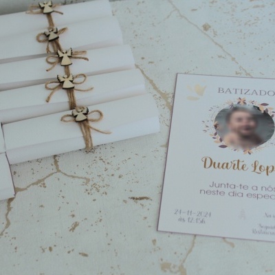 Convite para batizado com foto e texto em português sobre superfície clara, junto a rolos de papel amarrados com cordão.