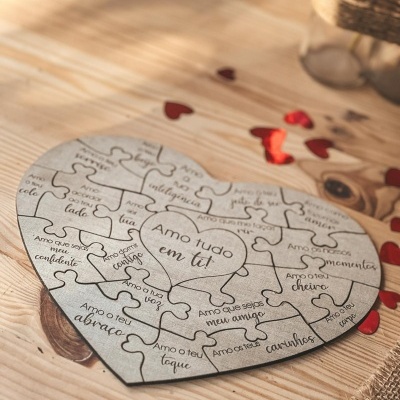 Puzzle de madeira em forma de coração com texto gravado em português sobre mesa de madeira com corações vermelhos.