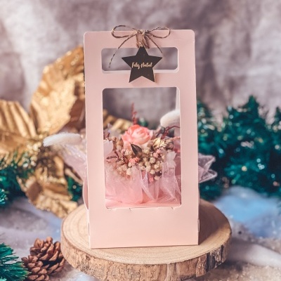 Caixa rosa com flores artificiais, etiqueta 'Feliz Natal' e base de madeira