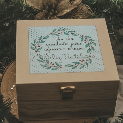 Caixa de madeira com etiqueta de Natal e fecho dourado, decorada e rodeada por elementos naturais de Natal