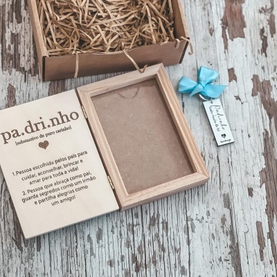 Moldura de madeira clara, cartão em português e fita azul com etiqueta sobre superfície envelhecida e caixa de papelão