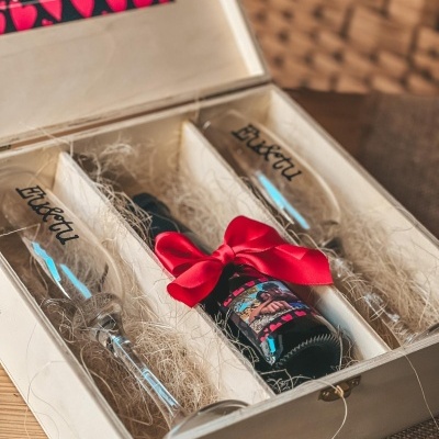 Caixa de madeira com duas taças de vidro e uma garrafa decorada com fita vermelha