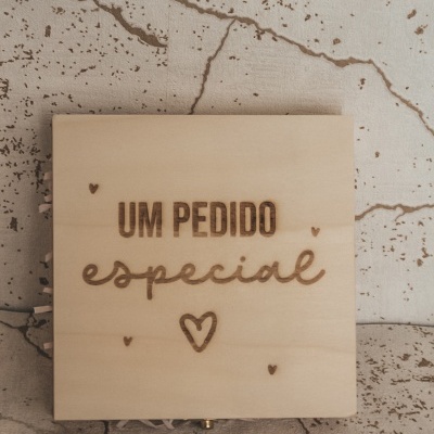 Caixa de madeira clara com texto gravado e corações sobre superfície com padrão de rachaduras