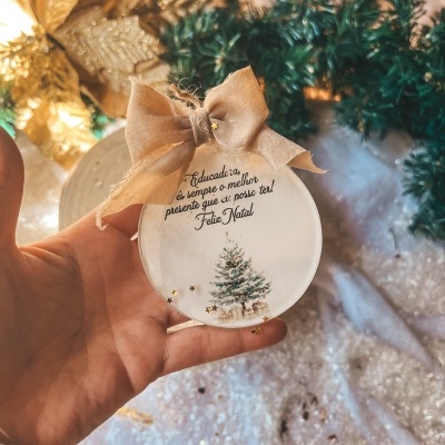 Ornamento redondo transparente com laço dourado e mensagem de Natal em português, decorado com árvore de Natal