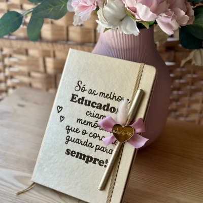 Caderno bege com caneta dourada e vaso rosa com flores artificiais