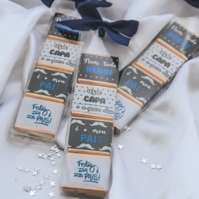 Barras de chocolate embrulhadas com texto comemorativo para Dia dos Pais sobre tecido branco e estrelas prateadas