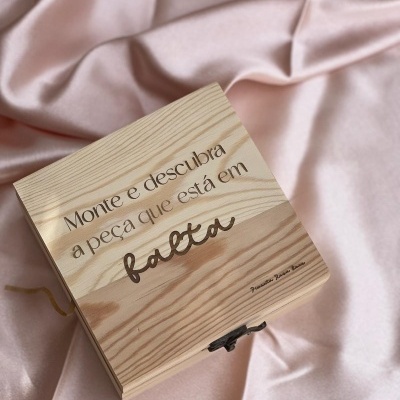 Caixa de madeira clara com inscrição em português sobre tecido rosa.