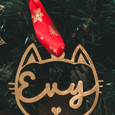 Enfeite de Natal de gato dourado pendurado em árvore com fita vermelha