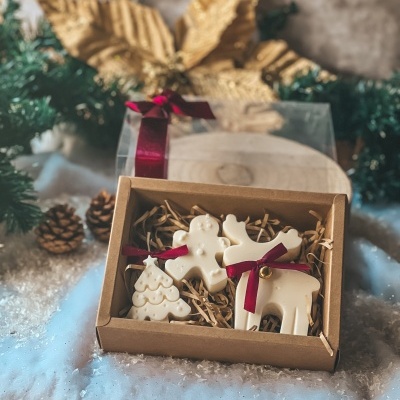 Três decorações de Natal brancas em caixa de cartão com laços vermelhos e decoração natalícia ao fundo