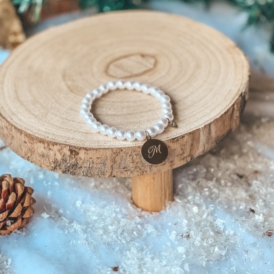 Pulseira de pérolas brancas com pendente dourado sobre madeira