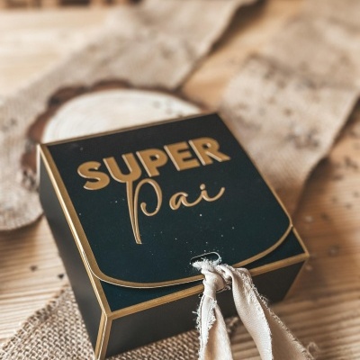 Caixa preta de presente com texto dourado SUPER Pai e fita de tecido bege.