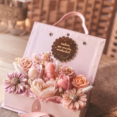Caixa rosa com flores artificiais e ursinho cor de rosa, etiqueta com texto escrito.