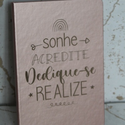Caderno rosa com texto motivacional dourado sobre azulejos claros