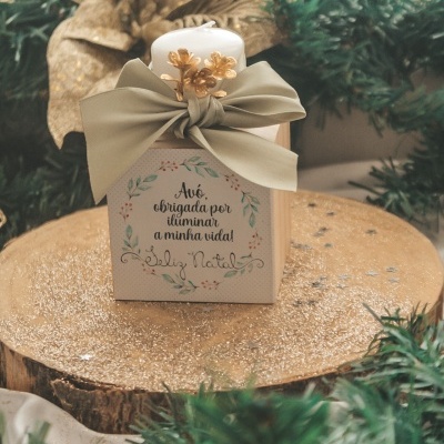 Caixa decorativa branca com vela, texto em português e laço bege em ambiente natalino