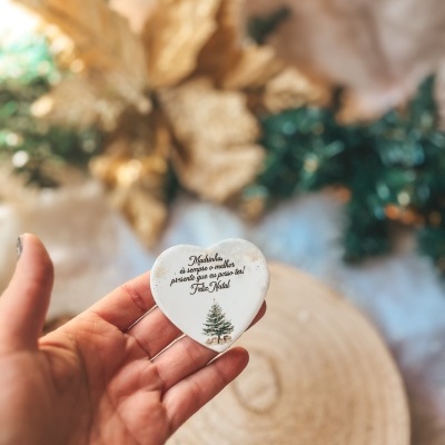 Objeto coração branco com texto natalício em mão sobre fundo decorado