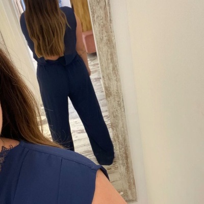 Macacão azul-escuro com detalhe em renda preta visto numa mulher junto a espelho rústico