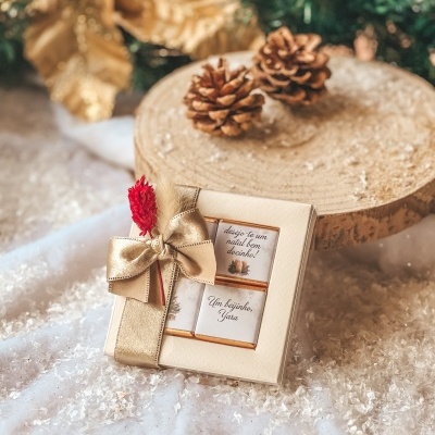 Caixa de chocolates embalagem bege com laço dourado e texto de Natal