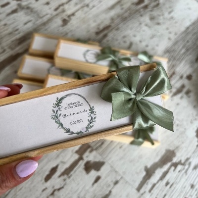 Caixa retangular de madeira clara com tampa branca, texto decorativo e laço verde