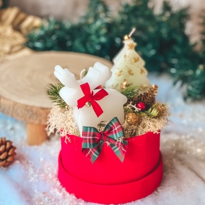 Caixa vermelha com laço, velas de rena e árvore de Natal, musgo e pinhas.