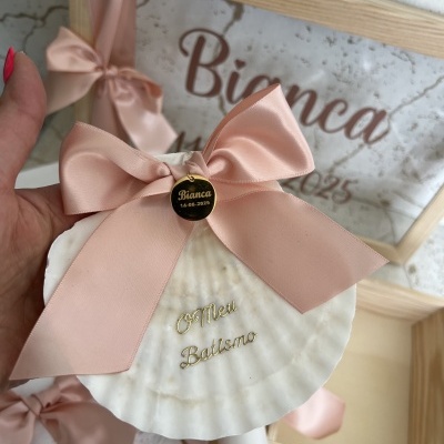 Concha decorativa com fita rosa e medalha preta gravada, fundo de caixa de madeira com texto