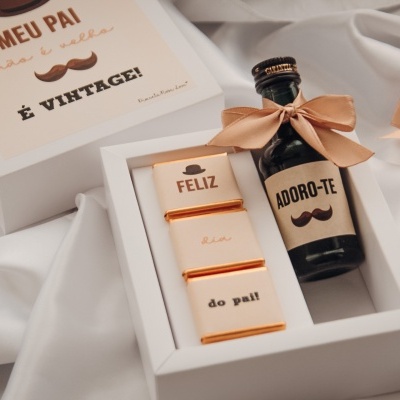 Caixa branca com garrafa e chocolates com mensagens para o pai em fundo de tecido branco