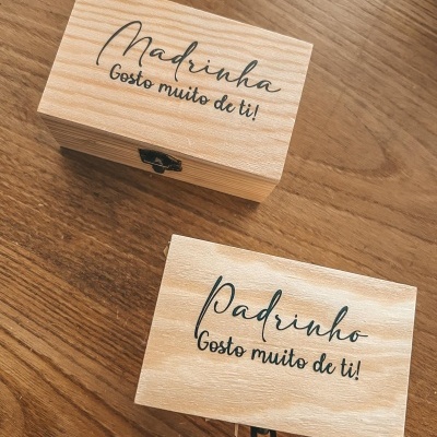 Duas caixas de madeira clara com inscrições para padrinho e madrinha sobre superfície de madeira.