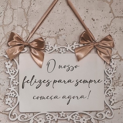 Placa decorativa branca com texto em português pendurada com fita e laços rosa dourado