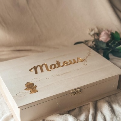 Caixa de madeira clara com nome Mateus em relevo dourado e anjo decorativo