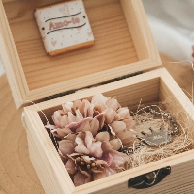 caixa de madeira clara aberta com flores artificiais e colar dentro