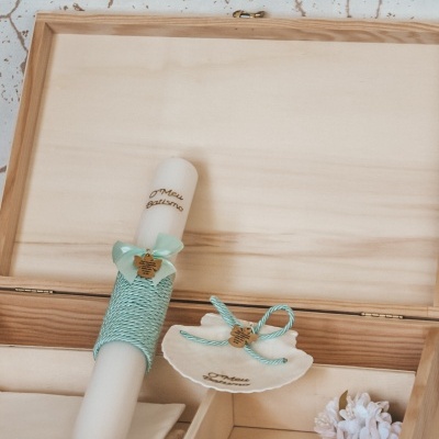 Caixa de madeira clara com vela decorada, prato branco e arranjo de flores