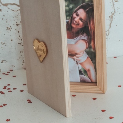 Moldura de madeira clara em forma de livro com fotografia e pequeno coração de madeira gravado
