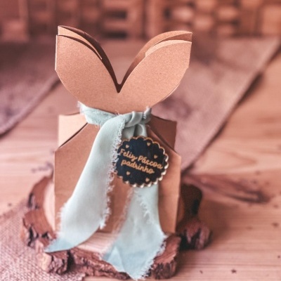 Caixa em cartão com formato de orelhas de coelho com fita azul e etiqueta de Páscoa.