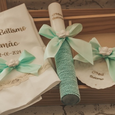 Conjunto para batismo com toalha, vela e porta-fraldas em branco com fitas verdes água e detalhes em renda numa caixa de madeira
