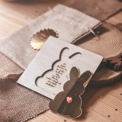 Cartão decorativo em forma de coelho com peça dourada e coração cor-de-rosa sobre mesa de madeira